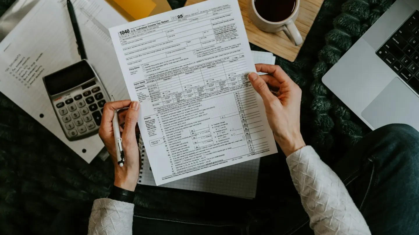 Hands holding tax forms with calculator and laptop